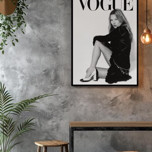 Puede incluir: Impresi&oacute;n en blanco y negro de una portada de la revista Vogue con una mujer con un vestido negro y tacones. El logo de Vogue est&aacute; en la parte superior. La impresi&oacute;n est&aacute; en un marco negro, exhibida en una pared gris texturizada con taburetes y una mesa de madera.