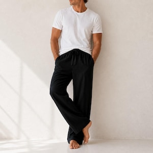 May include: A plain white short-sleeved crew neck t-shirt paired with solid black loose-fitting trousers. The trousers feature a drawstring waist with a visible tie and a wide-leg cut that falls straight to the floor, creating a relaxed silhouette.