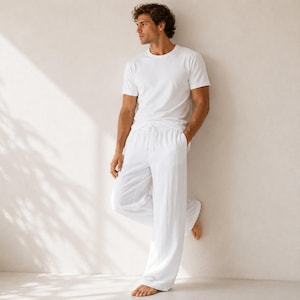 May include: A white short-sleeved crew neck t-shirt paired with matching white loose-fitting trousers featuring an adjustable drawstring waistband. The set is constructed from a lightweight, textured fabric, providing a clean, monochromatic appearance.