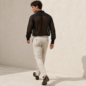 May include: A long-sleeved black shirt made of a sheer, translucent fabric with a classic collar and buttoned cuffs, paired with light beige trousers featuring a straight-leg cut, a waistband with belt loops, and black leather loafers.
