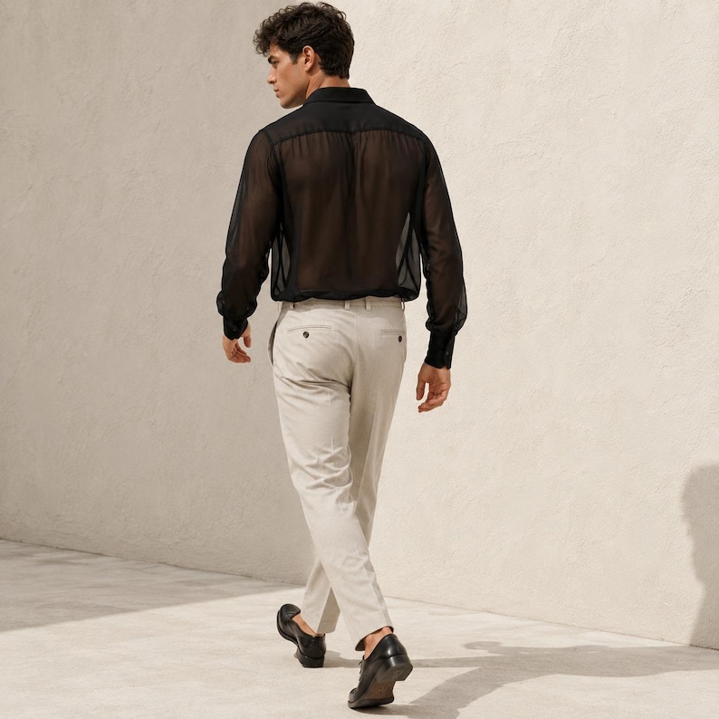 May include: A long-sleeved black shirt made of a sheer, translucent fabric with a classic collar and buttoned cuffs, paired with light beige trousers featuring a straight-leg cut, a waistband with belt loops, and black leather loafers.