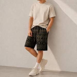 May include: A beige short-sleeve t-shirt paired with black shorts featuring a dark olive green geometric pattern. The shorts include an adjustable drawstring waistband and a relaxed fit. The outfit is completed with white athletic sneakers and socks.