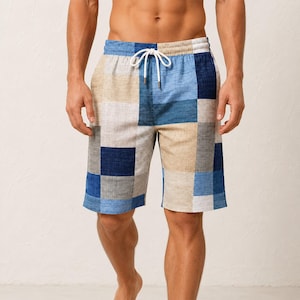 Puede incluir: Pantalones cortos con un patrón de patchwork de bloques rectangulares en azul, azul claro, beige y blanco. Los pantalones tienen una cintura elástica con un cordón blanco y un acabado de tela texturizada con líneas horizontales tejidas.