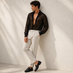 May include: A sheer black long-sleeved button-down shirt with a classic collar, paired with light beige pleated trousers featuring a straight-leg cut and a clean waistband, complemented by polished black leather loafers with a low heel.