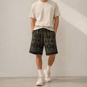 May include: A beige short-sleeve crew neck t-shirt paired with dark olive green and black patterned shorts featuring a geometric design and a drawstring waist. The outfit is completed with white crew socks and white athletic sneakers.