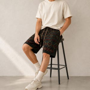 May include: A pair of shorts featuring a dark, multi-colored geometric pattern with red, green, and blue accents, paired with a plain cream-colored short-sleeved t-shirt, white crew socks, and light-colored athletic sneakers with laces.