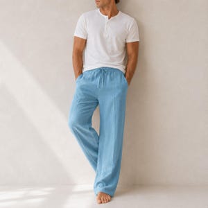 May include: A white short-sleeved henley shirt with a buttoned placket paired with light blue loose-fitting trousers featuring a drawstring waistband and a straight-leg cut. The clothing set is presented in a simple, clean, and neutral style.