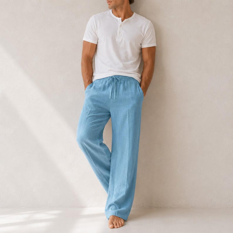 May include: A white short-sleeved henley shirt with a buttoned placket paired with light blue loose-fitting trousers featuring a drawstring waistband and a straight-leg cut. The clothing set is presented in a simple, clean, and neutral style.