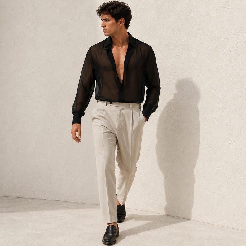 May include: A long-sleeved black sheer button-down shirt with a pointed collar and cuffed sleeves, paired with light beige pleated trousers that feature a straight-leg cut and a visible button closure at the waist, worn with black leather loafers.