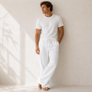 May include: A white short-sleeved crew neck t-shirt paired with matching white long trousers. The trousers feature a drawstring waistband and a relaxed, straight-leg fit. Both garments are made of a solid white fabric with a subtle texture.