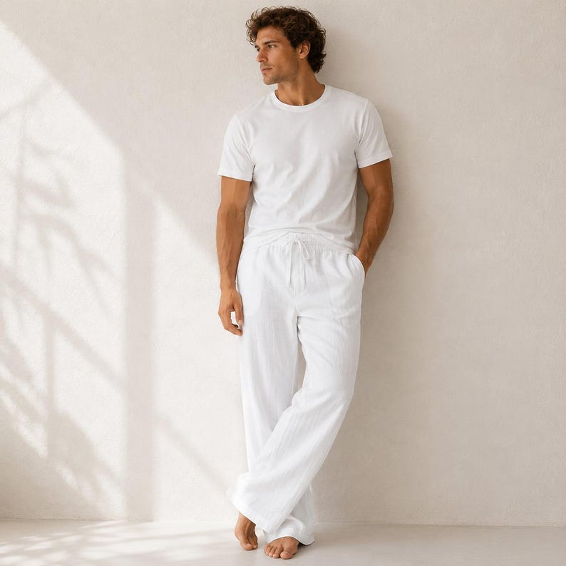 May include: A white short-sleeved crew neck t-shirt paired with matching white long trousers. The trousers feature a drawstring waistband and a relaxed, straight-leg fit. Both garments are made of a solid white fabric with a subtle texture.