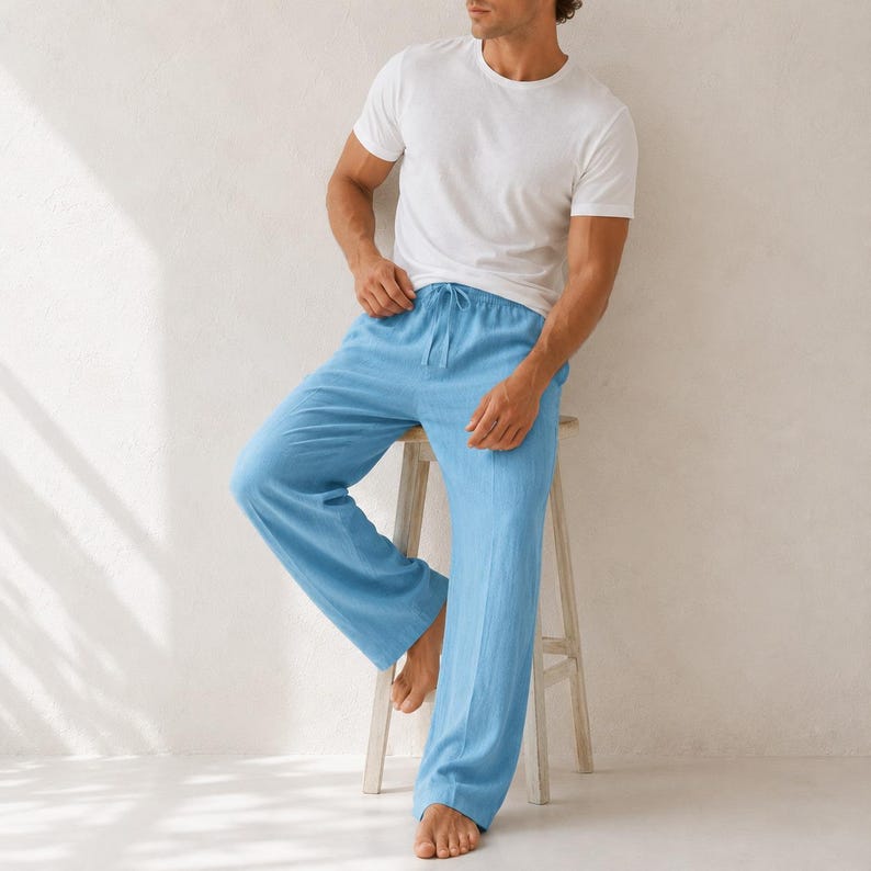 May include: A plain white short-sleeved crew neck t-shirt paired with loose-fitting light blue trousers featuring an elastic waistband with a drawstring tie. The trousers have a relaxed, straight-leg silhouette and are made of a textured fabric.