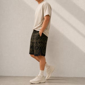 May include: A beige short-sleeve t-shirt paired with dark olive green shorts featuring a black geometric pattern. The shorts have a solid black side panel detail and a straight hemline. The outfit is completed with white athletic sneakers and white socks.