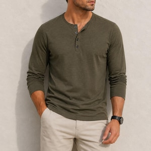 May include: An olive green long-sleeve henley shirt featuring a three-button placket and a textured fabric finish, paired with light beige trousers. The shirt has a round neckline and long sleeves, while the trousers are plain and neutral-toned.