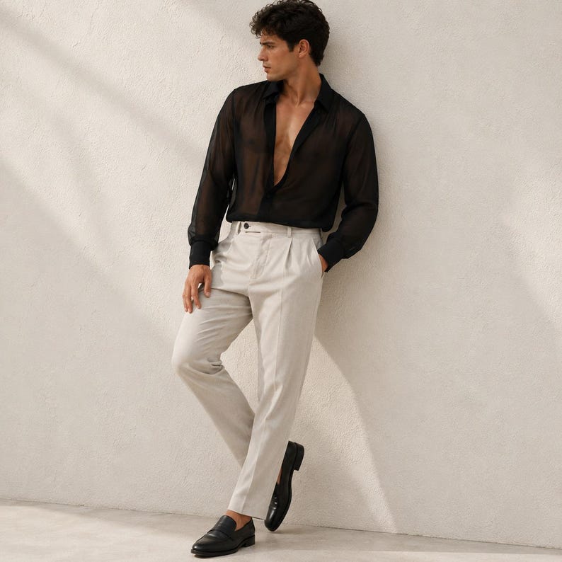 May include: A long-sleeved black shirt made of a sheer, translucent fabric with a deep V-neckline, paired with light beige trousers featuring a pleated front, a button closure, and a straight-leg cut, worn with black leather slip-on loafers.