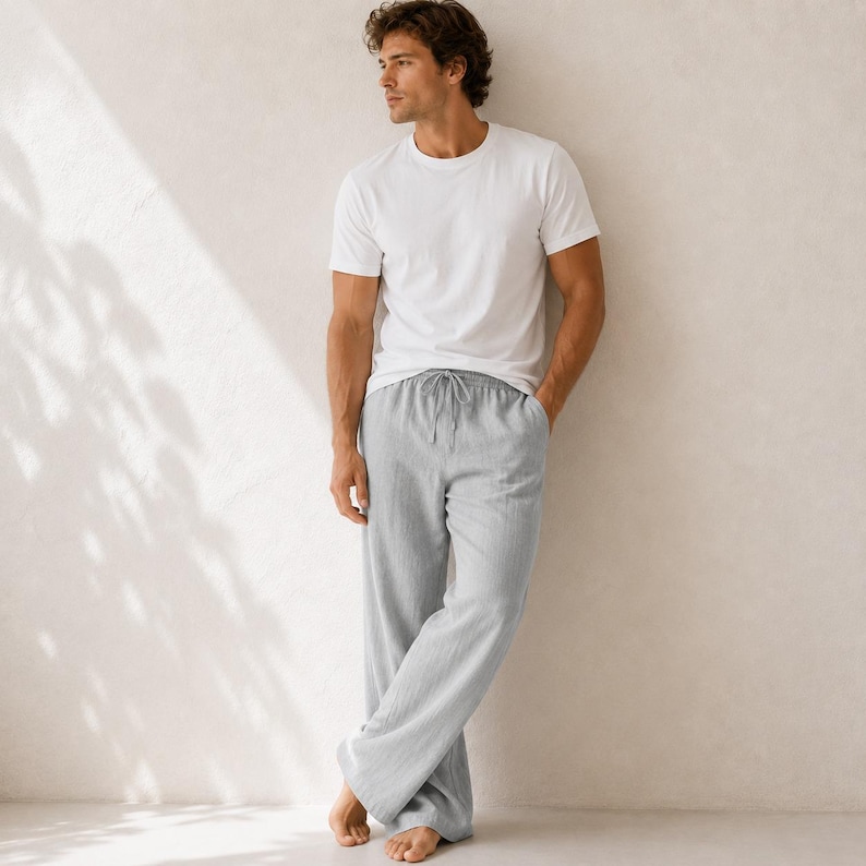 May include: A plain white short-sleeved crew neck t-shirt paired with loose-fitting light gray trousers. The trousers feature a drawstring waistband and a relaxed, straight-leg silhouette, providing a simple and clean look for casual wear.