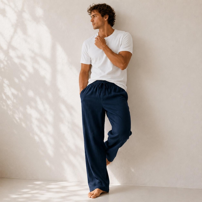 May include: A plain white short-sleeved crew neck t-shirt paired with loose-fitting navy blue trousers featuring an elasticized waistband with a drawstring tie. The trousers have a straight-leg cut and a solid dark blue color throughout.