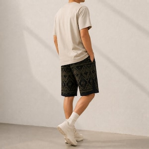 May include: A beige short-sleeved t-shirt paired with dark green shorts featuring a black geometric pattern. The shorts have a straight-leg cut and a solid black hem detail. The outfit is completed with white crew socks and white athletic sneakers.