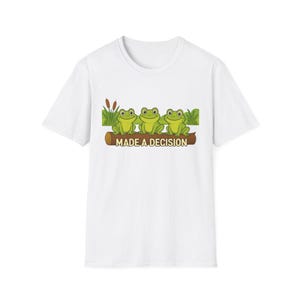 May include: White t-shirt featuring a graphic of three green cartoon frogs sitting on a log with the text "MADE A DECISION". The frogs are surrounded by green grass and cattails.