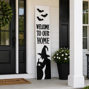 May include: A tall, rectangular white wooden porch sign featuring black silhouettes of three flying bats at the top, the black text "WELCOME TO OUR HOME" in the center, and a black silhouette of a witch stirring a cauldron at the bottom.