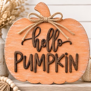 May include: A pumpkin-shaped wooden sign with a distressed orange finish, featuring the dark brown 3D text "hello PUMPKIN" and a decorative jute twine bow tied around the stem. The sign has a smooth, rounded edge and a flat surface.