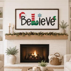May include: A rectangular wooden wall sign with a white shiplap background and a dark brown frame. The sign features the black text "Believe" with a red Santa hat on the B, a red and green striped elf boot as the l, a blue snowflake as the i, and holly.