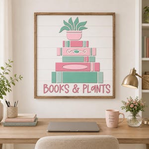 May include: A square wall art piece in a wooden frame featuring a white shiplap background. The design shows a stack of books in shades of pink and green, topped with a potted plant. The text "BOOKS & PLANTS" is printed in pink at the bottom.