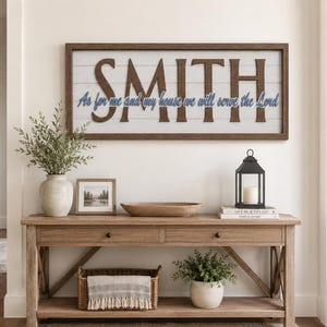 Op de afbeelding: Een rechthoekig wandbord met een donkerbruine houten lijst en witte horizontale latten. Het bord bevat de grote bruine tekst SMITH en de blauwe cursieve tekst As for me and my house we will serve the Lord op de witte achtergrond.