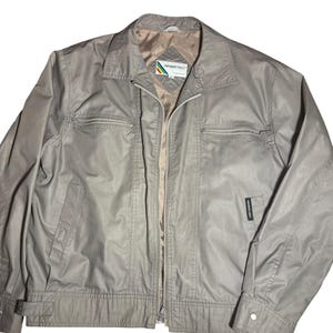 May include: A light grey jacket with a full zipper closure, two zippered chest pockets, and a small pocket on the left side. The jacket has a collared neckline and a light brown interior lining. The brand name "MEMBERS ONLY" is visible on the label.
