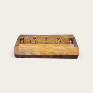 May include: A rectangular wooden wall-mounted shelf featuring a natural wood grain finish. The unit includes a lower storage compartment and an upper narrow ledge supported by four small, turned wooden spindles that connect the two sections.