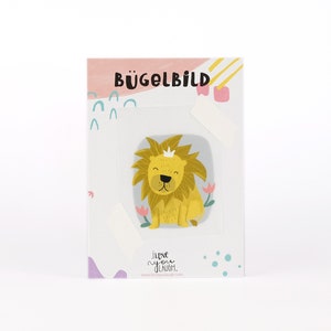 Può includere: Toppa da stirare con un simpatico leone di cartone animato che indossa una corona. Il leone è giallo e ha uno sfondo grigio chiaro con fiori rosa. Il testo "I love you a lot" è stampato sotto il leone.