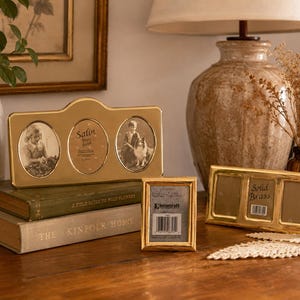 May include: A collection of three gold-toned brass picture frames. One horizontal triple-opening frame displays two black and white photos and a center label reading Satin Brass Frame. A vertical single frame and a horizontal triple frame are included.
