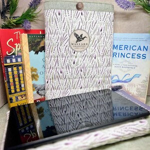 May include: A quilted fabric sleeve featuring a lavender sprig pattern, a light green top border with a single brown button, and a circular logo patch with a duck silhouette and the text Mallard Collective Distinctly Crafted.