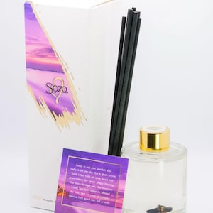 May include: A clear glass aromatherapy diffuser bottle with a gold cap, black reeds, and a white box with purple accents. The box and a card feature the brand name "Sozo" and inspirational text. The diffuser is designed for home fragrance.