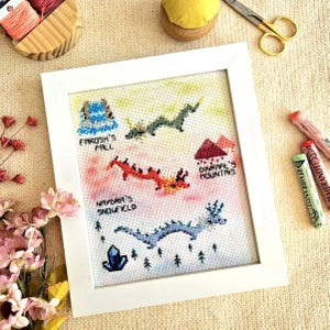 Pode incluir: Uma obra de arte em ponto cruz emoldurada com uma paisagem de fantasia com dragões e texto. A obra de arte inclui o texto "Fardsh's Fall", "Dinraal's Mountains" e "Naydra's Snowfield". Os dragões são verdes, vermelhos e azuis. A moldura é branca.