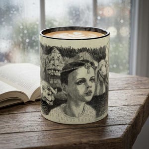 Peut inclure: Un mug en céramique orné d'une illustration détaillée au graphite représentant une personne portant une coiffe perlée, entourée de créatures fantastiques. Le mug possède un bord noir et contient une boisson avec un motif latte art en cœur.