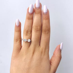 May include: A silver-toned ring featuring two distinct clear stones set side-by-side on a thin metal band. One stone is oval-shaped and the other is round-shaped, both positioned horizontally across the finger to create a balanced, open-style design.