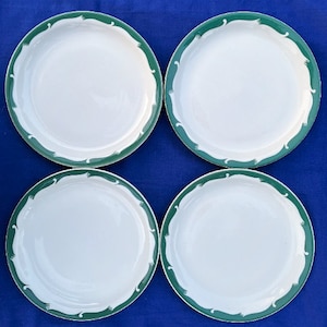 May include: Four white ceramic dinner plates with a green wavy border design.