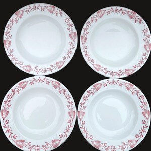 May include: Four white ceramic soup bowls with a red floral and leaf border design. The bowls have a wide rim and a deep center. The floral design includes stylized tulips and leaves. The bowls are arranged in a square formation.