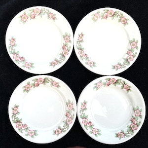 May include: Set of four white ceramic plates with a pink floral design. The plates have a scalloped edge and are perfect for serving desserts or appetizers.