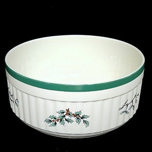 May include: A white ceramic bowl with a green rim and a holly and berry design. The bowl has a fluted edge and is perfect for serving holiday snacks or desserts.