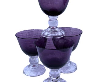 May include: Set of four purple glass goblets with clear glass stems and bases. The goblets have a textured surface.