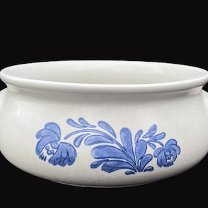 May include: A white ceramic bowl with two small handles and a blue floral design. The bowl has a wide, open top and a rounded body. The blue floral pattern is painted on the front of the bowl.