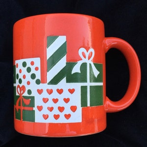 May include: A red ceramic mug with a Christmas-themed design. The mug features a pattern of green and white wrapped presents with red hearts and bows.