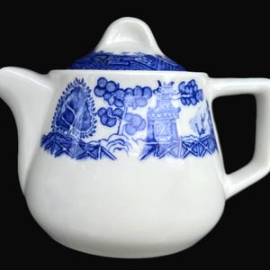 May include: A white ceramic teapot with a blue Willow pattern design. The teapot features a curved spout, a square handle, and a lid with a small knob. The blue pattern depicts trees, a pagoda, and other landscape elements.