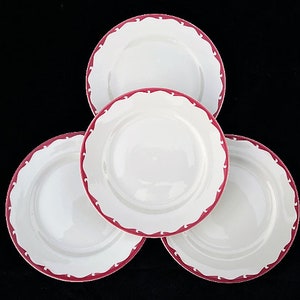 May include: Four white ceramic plates with a red scalloped edge. The plates are stacked on top of each other.