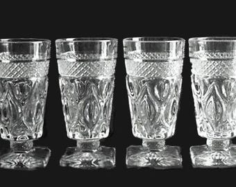May include: A set of four clear glass goblets featuring a textured diamond pattern around the upper rim and a vertical leaf-like embossed design on the main body. Each goblet stands on a short, thick stem with a square base for stability.