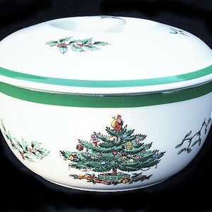 May include: White ceramic serving bowl with a lid, featuring a green band around the rim and handles. The bowl is decorated with a Christmas tree, Santa Claus, and holly and mistletoe sprigs. A festive holiday serving dish.