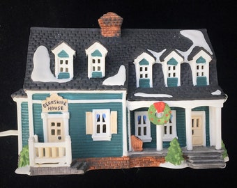 May include: A miniature ceramic house figurine painted teal with white trim, a dark gray shingled roof with snow accents, and a brick chimney. A sign above the front door reads BERKSHIRE HOUSE. The house features a front porch with a green wreath.