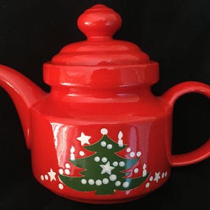 May include: Red ceramic teapot with a green Christmas tree design and white stars and candles.